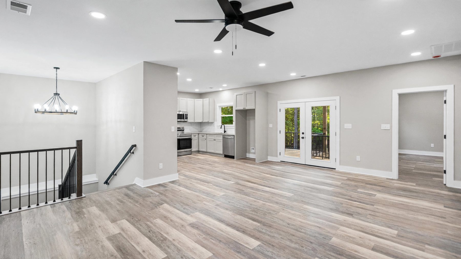 Open great room with an iron chandelier, stair railing and kitchen beyond at Raven's Ridge