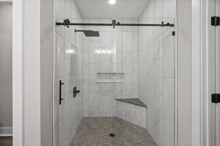 Walk-in tile shower with a corner bench and glass door at Hillcrest at Woodrun